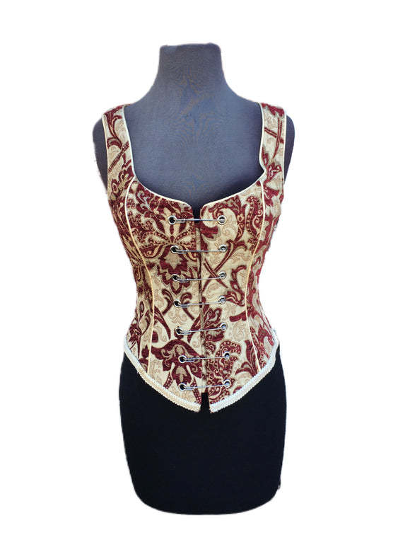 A Shrine classic!! A heavily constructed corset top in rich burgundy and ivory tapestry fabric with a great form fit. Heavy metal boning at sides and lycra stretch panel at back adds extra strong support. Fastens in front with seven large kilt pins but also zips in back for easy access. Rich ivory satin piping around armholes and neckline and ivory satin lining inside. Trimmed at the bottom with braided trim. This is one of our favorites! A very flattering fit. 